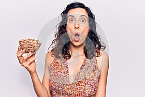 Young beautiful hispanic woman holding cornflakes scared and amazed with open mouth for surprise, disbelief face
