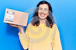 Young beautiful hispanic woman holding delivery package looking positive and happy standing and smiling with a confident smile