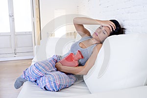 Young beautiful hispanic woman holding hot water bottle against belly suffering menstrual period pain