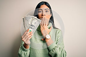 Young beautiful hispanic woman holding a pack of one dollar bunch of dollars cover mouth with hand shocked with shame for mistake,