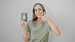 Young beautiful hispanic woman holding passport smiling happy and positive, thumb up doing excellent and approval sign over