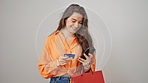 Young beautiful hispanic woman holding shopping bags using smartphone and credit card over isolated white background