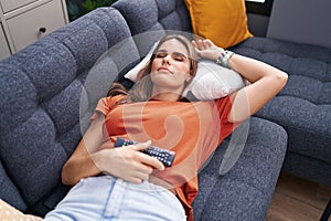 Young beautiful hispanic woman holding tv remote control lying on sofa sleeping at home