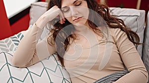 Young beautiful hispanic woman holding tv remote control lying on sofa sleeping at home