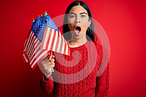 Young beautiful hispanic woman holding United States of American flag at independence day scared in shock with a surprise face,