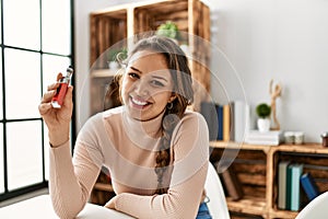 Young beautiful hispanic woman holding vaper sitting on table at home photo