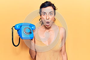 Young beautiful hispanic woman holding vintage telephone scared and amazed with open mouth for surprise, disbelief face