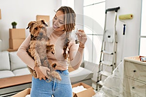 Young beautiful hispanic woman hugging dog holding key at new home