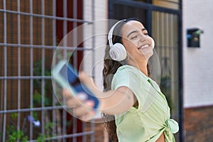 Young beautiful hispanic woman listening to music and dancing at street