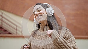 Young beautiful hispanic woman listening to music and dancing at street