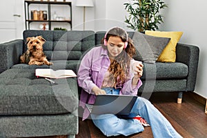 Young beautiful hispanic woman listening to music sitting on floor with dog at home