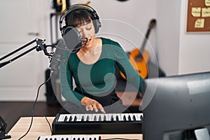 Young beautiful hispanic woman musician singing song playing piano at music studio