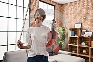 Young beautiful hispanic woman musician smiling confident holding violin at home