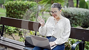 Young beautiful hispanic woman on an online meeting with laptop sitting on a bench at the park