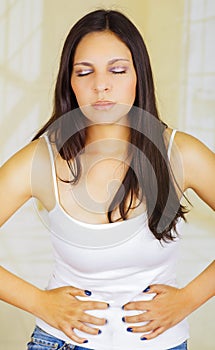 Young beautiful hispanic woman in painful expression touching her belly with both hands, suffering menstrual period pain