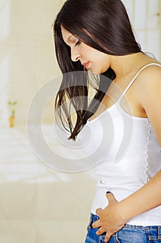 Young beautiful hispanic woman in painful expression touching her belly, suffering menstrual period pain, female health