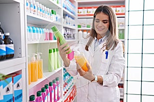 Young beautiful hispanic woman pharmacist holding shampoo bottles at pharmacy