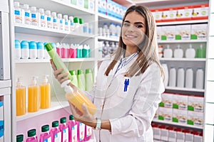 Young beautiful hispanic woman pharmacist holding shampoo bottles at pharmacy