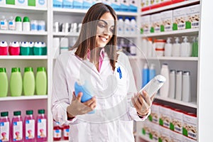 Young beautiful hispanic woman pharmacist holding shampoo bottles at pharmacy