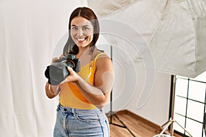 Young beautiful hispanic woman photographer holding professional camera photo studio