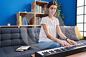 Young beautiful hispanic woman playing piano sitting on sofa at park