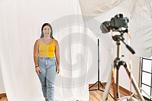 Young beautiful hispanic woman posing as model at photography studio sticking tongue out happy with funny expression