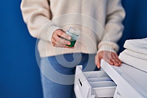 Young beautiful hispanic woman pouring detergent on washing machine at laundry room