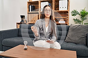 Young beautiful hispanic woman psychologist sitting on sofa speaking at psychology clinic