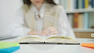 Young beautiful hispanic woman reading book turning next page at university classroom