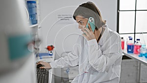Young, beautiful hispanic woman scientist earnestly immersed in a tech-filled conversation on smartphone while working on computer