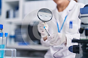 Young beautiful hispanic woman scientist looking test tube with loupe at laboratory