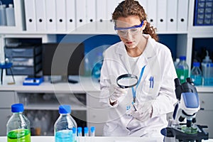 Young beautiful hispanic woman scientist looking test tube with loupe at laboratory