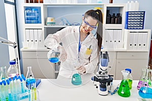 Young beautiful hispanic woman scientist pouring liquid on test tube at laboratory