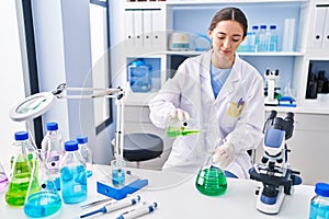 Young beautiful hispanic woman scientist pouring liquid on test tube at laboratory