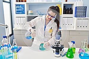 Young beautiful hispanic woman scientist pouring liquid on test tube at laboratory