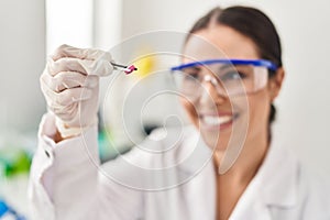Young beautiful hispanic woman scientist smiling confident holding pill at laboratory