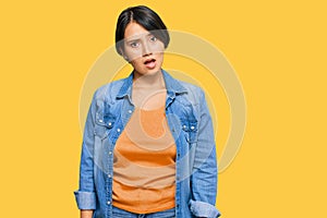 Young beautiful hispanic woman with short hair wearing casual denim jacket in shock face, looking skeptical and sarcastic,