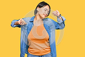 Young beautiful hispanic woman with short hair wearing casual denim jacket stretching back, tired and relaxed, sleepy and yawning
