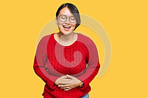 Young beautiful hispanic woman with short hair wearing casual sweater and glasses smiling and laughing hard out loud because funny