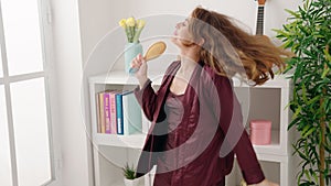 Young beautiful hispanic woman singing song using brush as a microphone at bedroom