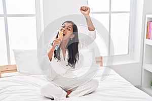 Young beautiful hispanic woman singing song using brush as a microphone at bedroom