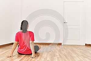 Young beautiful hispanic woman sitting on floor on back view at empty room