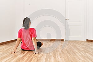 Young beautiful hispanic woman sitting on floor on back view at empty room