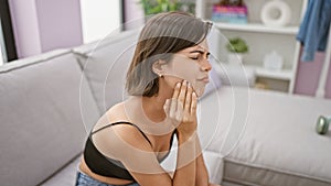 Young beautiful hispanic woman sitting on sofa suffering for toothache at home