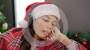 Young beautiful hispanic woman sleeping on sofa by christmas tree wearing headphones at home