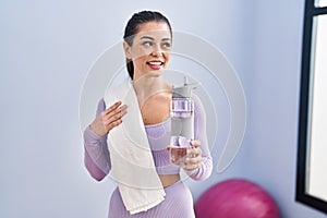 Young beautiful hispanic woman smiling confident holding bottle of water at sport center