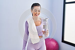 Young beautiful hispanic woman smiling confident holding bottle of water at sport center