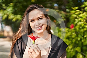 Young beautiful hispanic woman smiling confident holding flower at park