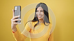 Young beautiful hispanic woman smiling confident making selfie by the smartphone over isolated yellow background