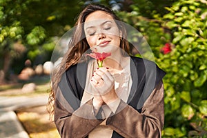 Young beautiful hispanic woman smiling confident smelling flower at park